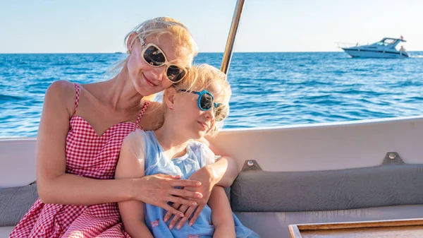 Sonriendo se sientan dos chicas en un yate, un adulto con un aspecto carismático, una sonrisa feliz joven en el horizonte del mar, el concepto de comparación en gafas monocromas durante el día, ambos —  Fotos de Stock