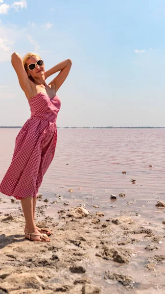 Ragazza allegra in un bel vestito, giovane con un aspetto carismatico sullo sfondo di un lago rosso con nuvole blu in una giornata estiva — Foto Stock