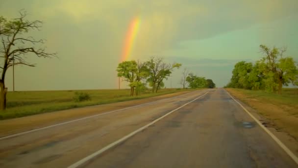 Arco iris en la carretera, monta un coche en la carretera y ver un gran puente multicolor romántico, alrededor de los árboles — Vídeo de stock