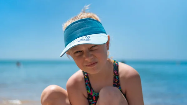Una chica en el mar se sienta en la playa en verano en el agua azul, el fondo es hermoso —  Fotos de Stock