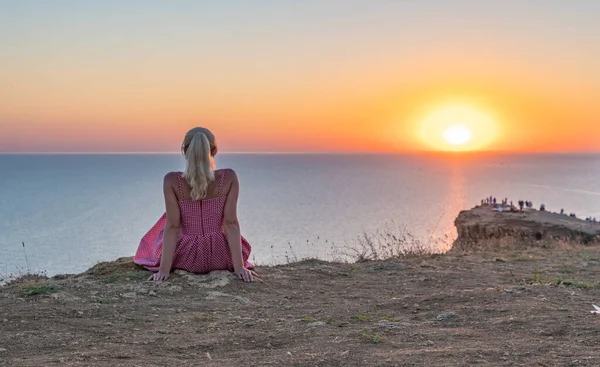 Una ragazza allegra con un bell'aspetto guarda il tramonto con la schiena in estate la sera — Foto Stock