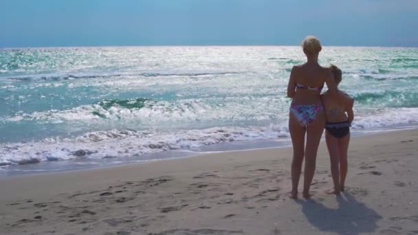 Mädchen stehen und schauen mit dem Rücken auf das Meer, kuscheln Mutter und Tochter mit Blick auf das Wasser von der Seite — Stockvideo