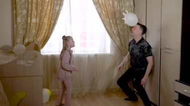 Ev kıyafetleriyle büyük bir oturma odasında küçük güzel bir kızla neşeli taşaklar. Beşiğe ve kanepeye yaslan..