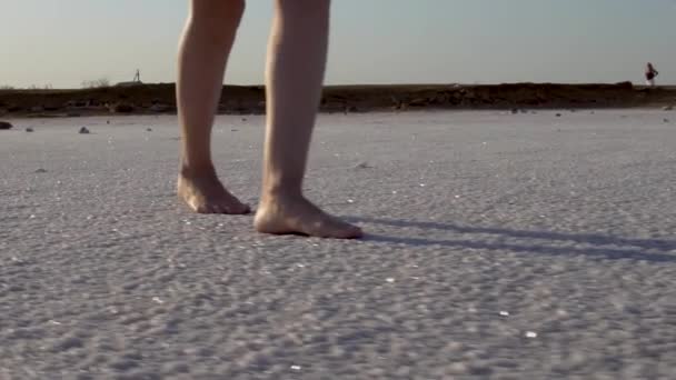 Une fille marche sur un lac salé recouvert de sel de cristal en été, pieds nus — Video