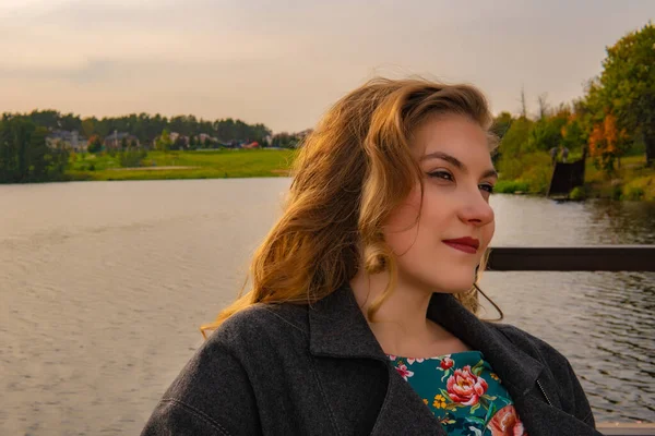 美しい女性午後には桟橋の秋にコートで素敵な笑顔で池の近くに立って — ストック写真
