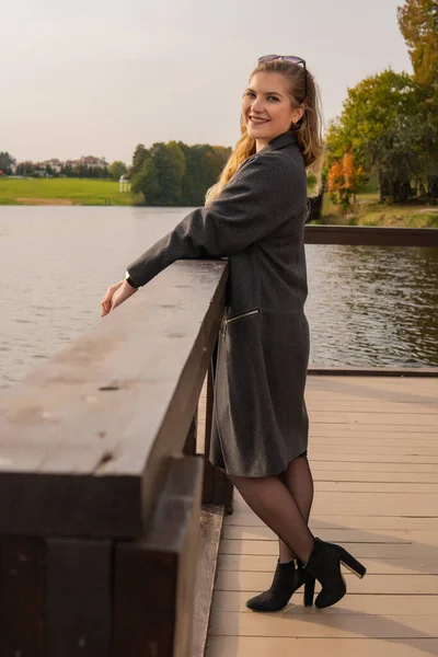 Happy young stand near the pond with a charismatic appearance with a great appearance in a coat in the fall on the moler in the afternoon — Stock fotografie