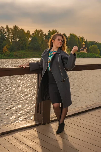幸せな大人の女性白い肌の優しい表情で池の近くに立ち、秋には桟橋の上にコートを着て午後 — ストック写真