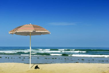 Plaj güneş kalkan şemsiye ve parmak arası terlik okyanus su kenarında