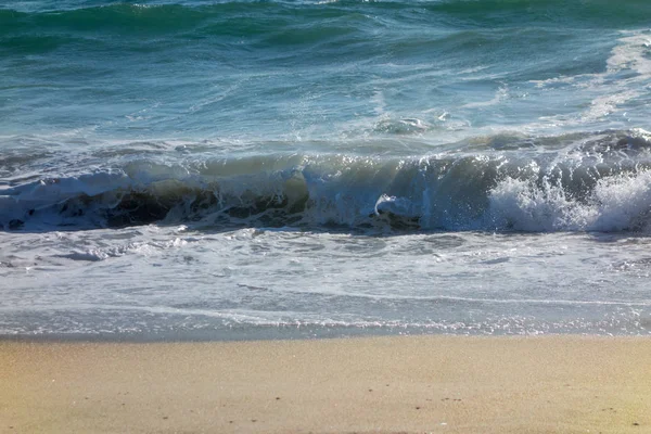 強力な圧延の海の波により平坦化した黄色の砂が濡れています — ストック写真