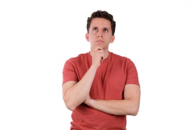 Düşünceli bir genç adam, elleri çenesinde, analiz ediyor, beyaz arka planda kırmızı bir tişört giyiyor. Yukarı bakıyorum.