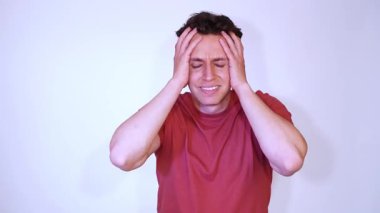 Başı çok kötü ağrıyan korkmuş bir adam, kafasına dokunuyor, beyaz arka planda izole edilmiş kırmızı bir tişört giyiyor.