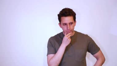 Düşünceli bir genç adam, elleri çenesinde, analiz ediyor, beyaz arka planda yeşil bir tişört giyiyor..