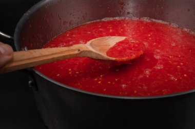 Taze domates püresiyle ahşap kaşığı kapatarak ev yapımı organik sebze hazırlama ve sağlıklı besin konseptini metal tencereyle kaplayın.