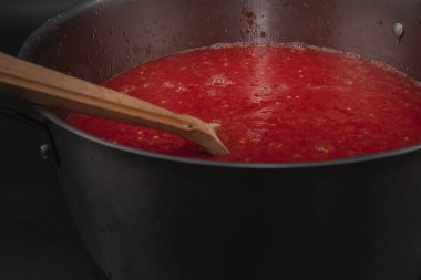 Taze domates püresiyle ahşap kaşığı kapatarak ev yapımı organik sebze hazırlama ve sağlıklı besin konseptini metal tencereyle kaplayın.