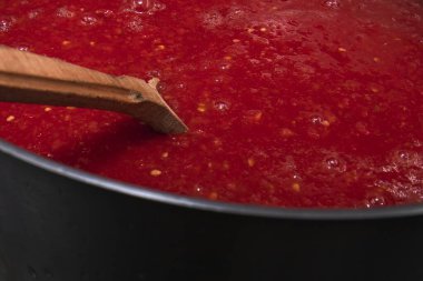 Taze domates püresiyle ahşap kaşığı kapatarak ev yapımı organik sebze hazırlama ve sağlıklı besin konseptini metal tencereyle kaplayın.