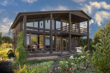 İki katlı modern ahşap ev yeşil bahçe ve bitki konseptiyle çevrili büyük panoramik pencereli kırsal yaşam tarzı ve sürdürülebilir mimari