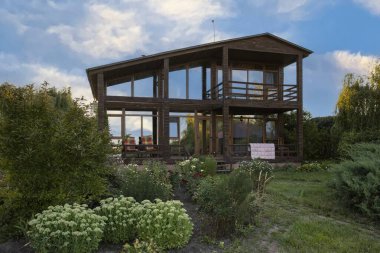 İki katlı modern ahşap ev yeşil bahçe ve bitki konseptiyle çevrili büyük panoramik pencereli kırsal yaşam tarzı ve sürdürülebilir mimari