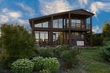 İki katlı modern ahşap ev yeşil bahçe ve bitki konseptiyle çevrili büyük panoramik pencereli kırsal yaşam tarzı ve sürdürülebilir mimari