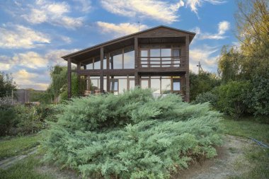 İki katlı modern ahşap ev yeşil bahçe ve bitki konseptiyle çevrili büyük panoramik pencereli kırsal yaşam tarzı ve sürdürülebilir mimari