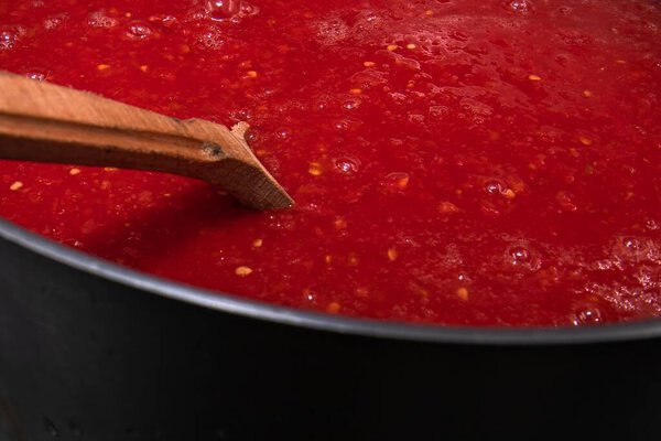 Крупный план деревянной ложки со свежим томатным пюре над металлическим горшком концепции домашней приготовления органических овощных препаратов и здоровой пищи