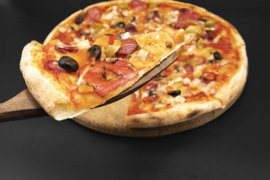 Eritilmiş peynirli, zeytinli, sebzeli ve salamlı, ahşap spatulada servis edilen bir dilim pizzayı kapat.