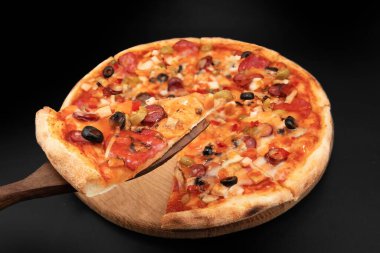 Eritilmiş peynirli, zeytinli, sebzeli ve salamlı, ahşap spatulada servis edilen bir dilim pizzayı kapat.