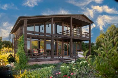 Çevresi yeşil bahçe ve çiçeklerle çevrili iki katlı modern ahşap ev rahat kırsal bir ortam yaratıyor.