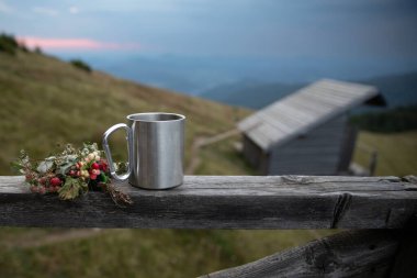 Ahşap çitin üzerinde metal kamp kupası ve yabani böğürtlenler dağ kulübesi ve manzaralı arka plan konsepti doğa yürüyüşü yaşam tarzı ve kırsal doğa rahatlaması.