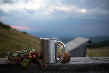 Yabani böğürtlenli metal kamp kupası ve ahşap çitin üzerindeki fındık dağ kulübesi ve doğa doğa ve eko turizmine karşı doğa yürüyüşü konsepti.