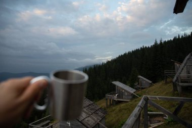 El ele tutuşan metal kamp kupası ve dağ manzarası. Arka planda seyahat macerası. Sabah kahvesi, açık hava yaşam tarzı ve kamp yapma kavramı.