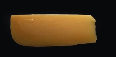 Siyah arka plana peynir kaması yerleştirilmiş. Yakın plan. Süt ürünleri, gurme ürünleri, sağlıklı beslenme ve yemek malzemeleri kavramı..