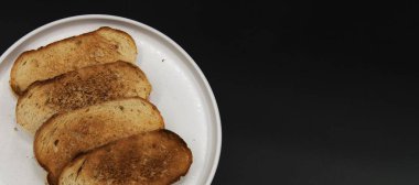 Koyu arkaplanlı beyaz tabakta servis edilen kızarmış ekmek dilimleri. Kahvaltı, aperatif, basit yemek ve fırın yemeği kavramı.