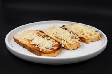 Beyaz tabakta rendelenmiş peynirle kaplı kızarmış ekmek dilimleri. Basit ev yapımı aperatif ya da aperatif, kahvaltı, yemek pişirme, yemek tarifleri ve menü tasarımı için ideal..