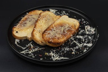Eritilmiş peynirli kızarmış ekmek ve siyah bir tabakta rendelenmiş parmesan biber serpiştirilmiş. Lezzetli ev yapımı aperatif, kahvaltı, yemek tarifleri ve menü tasarımı için ideal..