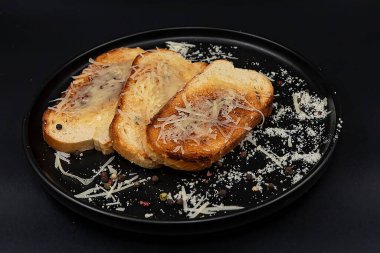 Eritilmiş peynirli kızarmış ekmek ve siyah bir tabakta rendelenmiş parmesan biber serpiştirilmiş. Lezzetli ev yapımı aperatif, kahvaltı, yemek tarifleri ve menü tasarımı için ideal..