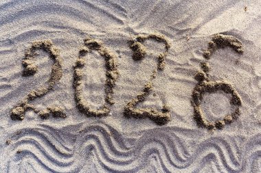 Parlak kumsalda, dekoratif dalga desenleriyle yazılmış 2026 sayıları. Yeni yıl kutlaması, tatil, seyahat ve tatil sezonu kavramı.