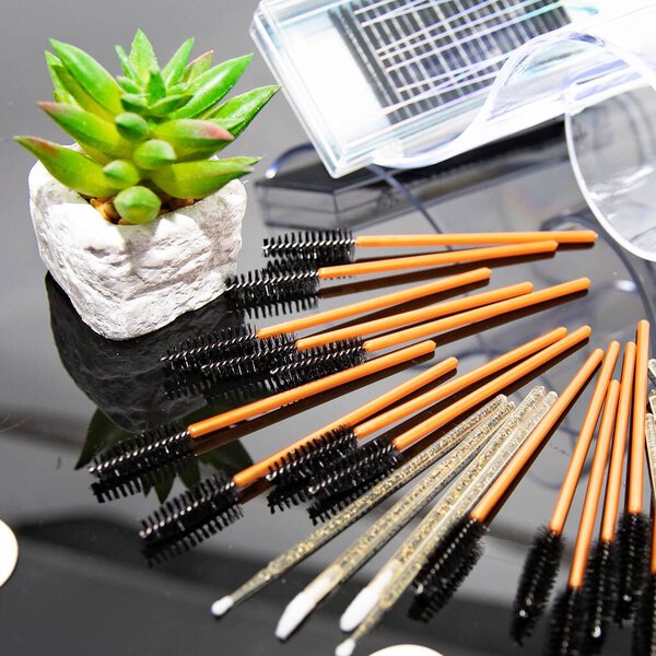 Набор одноразовых щёток для ресниц и белых подглазных пятен на глянцевой черной поверхности. Концепция красоты, наращивание ресниц, профессиональные салонные инструменты и косметический уход.
