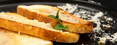 Üzeri erimiş peynirle kaplı, siyah tabakta peynir kırıntıları ve biberle kaplı kızarmış ekmek. Kahvaltı, atıştırmalık, ev yapımı yemek ve gurme aperatifi..