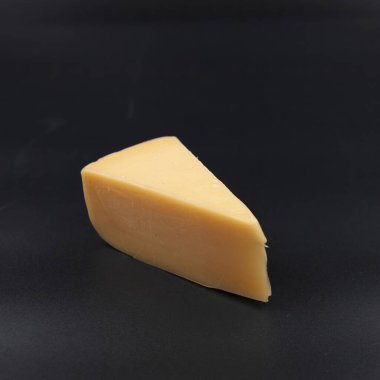 Siyah arkaplana yerleştirilmiş bir parça sarı peynir. Süt ürünleri, sağlıklı yiyecekler, yemek malzemeleri ve gurme besin konsepti.