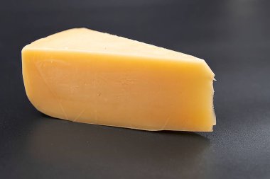 Siyah arkaplana yerleştirilmiş bir parça sarı peynir. Süt ürünleri, sağlıklı yiyecekler, yemek malzemeleri ve gurme besin konsepti.