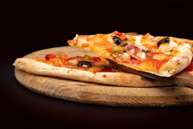 Eritilmiş peynirli, zeytinli, sosisli ve sebzeli sıcak pizza dilimini ahşap bir tahtaya yakın. Restoran menüsü, yemek servisi, İtalyan mutfağı ve fast food konseptleri için mükemmel..