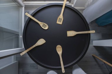 Yuvarlak siyah tepsiye dizilmiş kaşık ve spatulaları da içeren ahşap mutfak aletleri, ev ve restoran kullanımı için pişirme araçları, üst görünüm.