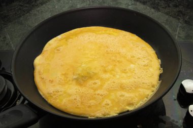 Fırının üstünde siyah bir tavada kızartılmış taze omlet yakın. Kahvaltı, yemek pişirme, ev yapımı yemek, sağlıklı yemek ve aşçılık hazırlıkları için mükemmel..