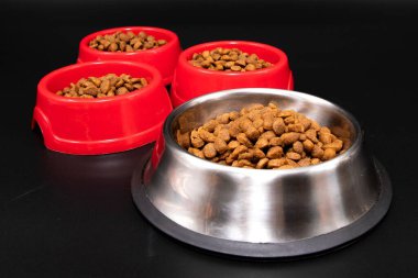 Paslanmaz çelik ve kırmızı kâseleri kapayın. Siyah arka planda kuru hayvan mamasıyla birlikte. Kedi ve köpek beslenme, hayvan bakımı ve sağlıklı beslenme kavramı.