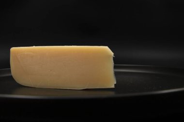 Siyah tabakta koyu arkaplanlı sert sarı peynir dilimi. Süt ürünleri, gurme yiyecekler, yemek malzemeleri ve sağlıklı beslenme kavramı..