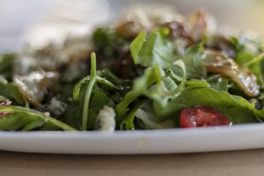 Taze roka, kavrulmuş armut dilimleri, mavi peynir parçaları, vişneli domatesler ve susamlı tohumlardan oluşan, beyaz bir tabakta servis edilen gurme salatasının yakın çekimi. Sağlıklı yemek, restoran yemeği ve diyet konsepti..