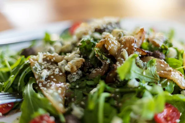 Taze roka, kavrulmuş armut dilimleri, mavi peynir parçaları, vişneli domatesler ve susamlı tohumlardan oluşan, beyaz bir tabakta servis edilen gurme salatasının yakın çekimi. Sağlıklı yemek, restoran yemeği ve diyet konsepti..