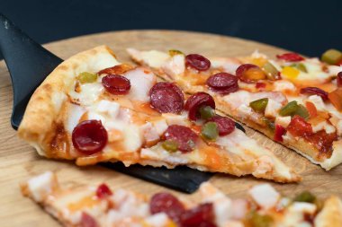 Appetizing slices of pizza with sausage, cheese, and vegetables served on a wooden board. Concept of Italian cuisine, fast food, and takeaway meal.