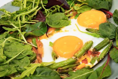 Yakın plan yumurta sarısı, yeşil fasulye, mısır ve tavada taze salata yaprakları. Lezzetli ev yapımı kahvaltı, protein yiyeceği, sağlıklı beslenme ve pişirme konsepti..