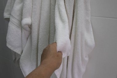 Banyoda asılı duran yumuşak beyaz bir pamuk havluyu tutan bir elin yakın çekimi. Temizlik, hijyen, günlük rutin, spa ve ev konforu kavramı.